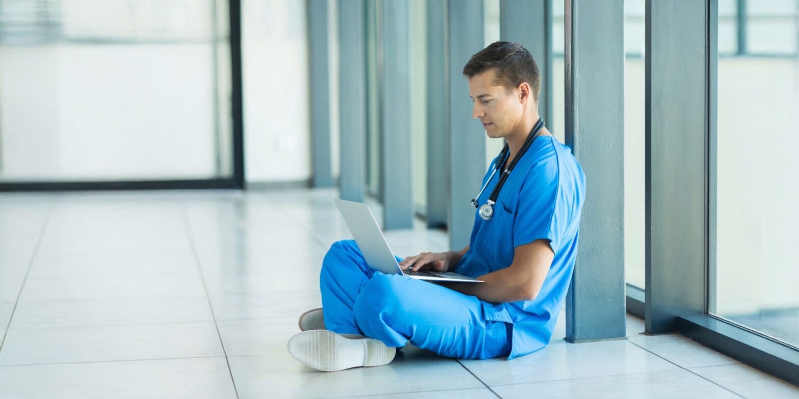 Gründungsberatung für junge Ärzte - der Weg zur eigenen Praxis. Junger Arzt mit Laptop auf dem Schoß.